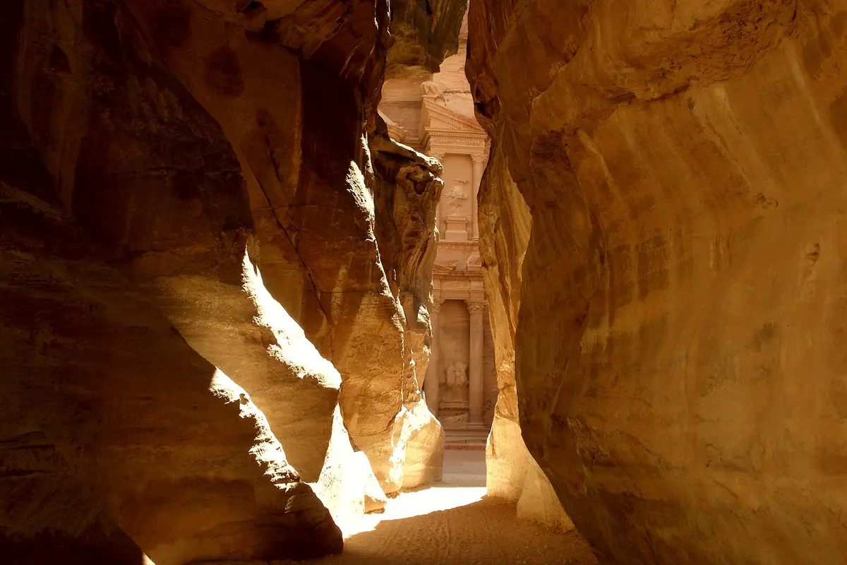 Looking down the narrow sandstone gorge of the Siq in Petra, with the carved facade of the Treasury lit up at the far end